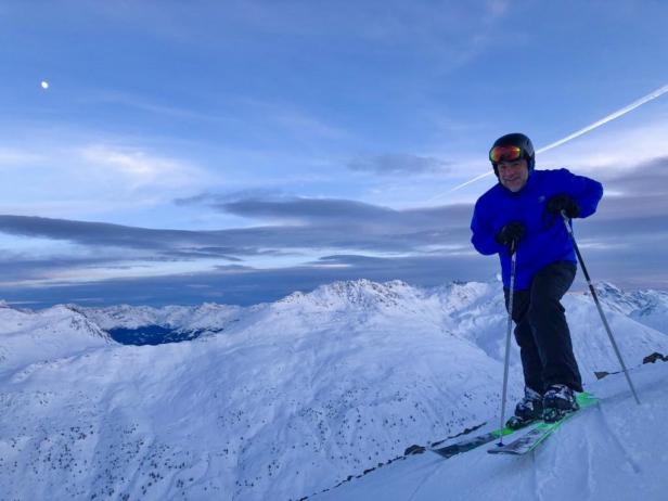 Ein Mann fährt Ski auf einem schneebedeckten Berg mit Blick auf eine Bergkette.
