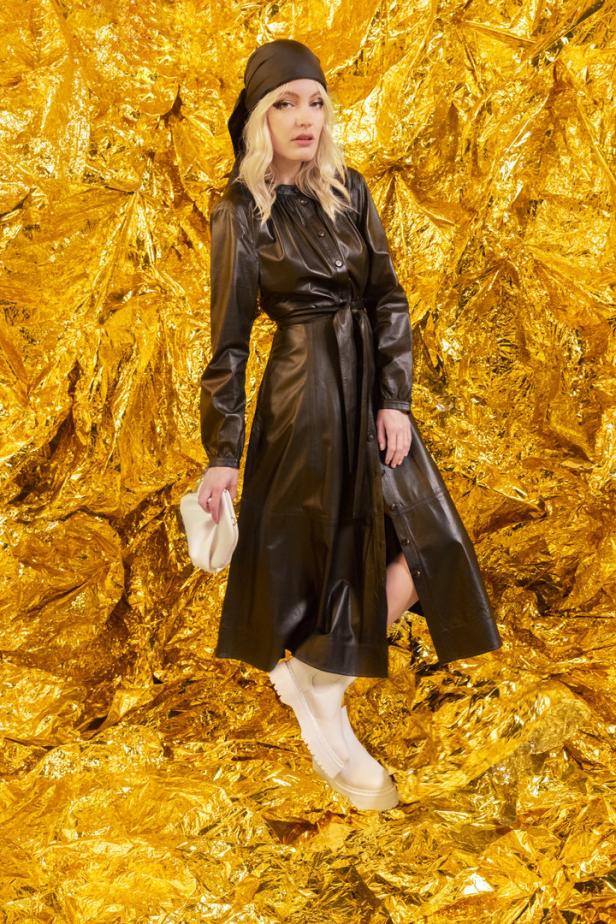 Eine Frau mit Kopftuch und schwarzem Ledermantel posiert vor einem goldenen Hintergrund.