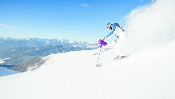 Ein Skifahrer fährt auf einer schneebedeckten Piste mit Blick auf die Berge.