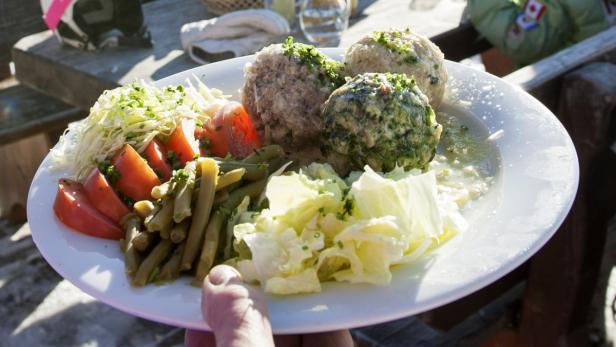 Ein Teller mit Knödeln, Salat und grünen Bohnen wird von einer Hand gehalten.