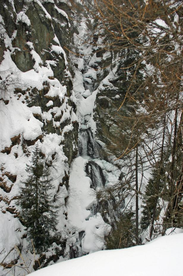 Ein kleiner Wasserfall fließt über einen schneebedeckten Felsen.