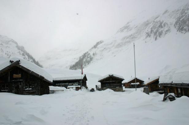 Mehrere schneebedeckte Holzhütten in einer winterlichen Berglandschaft.