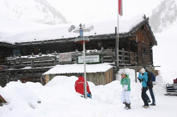Eine Gruppe von Menschen steht vor einer schneebedeckten Hütte im Winter.