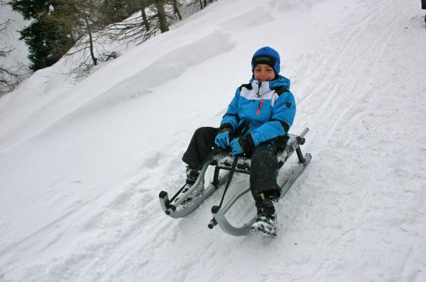 Ein Kind fährt mit einem Schlitten einen schneebedeckten Hügel hinunter.