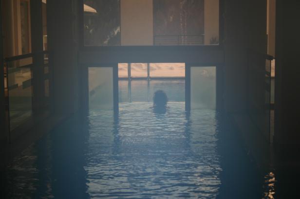 Eine Person schwimmt in einem Innenpool mit Blick auf den Sonnenuntergang.