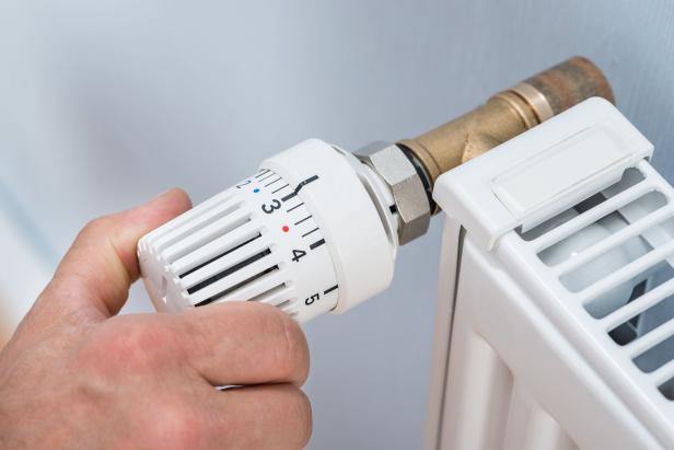 Person dreht am Thermostat des Heizkörpers