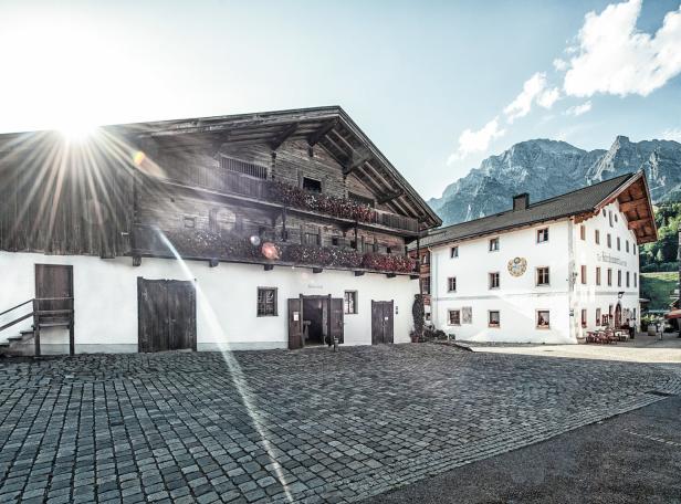 Ein traditionelles bayerisches Bauernhaus mit blumengeschmückten Balkonen vor einer Bergkulisse.