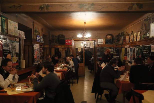 Gäste sitzen an Tischen in einem traditionellen Wiener Restaurant mit alten Postern an den Wänden.
