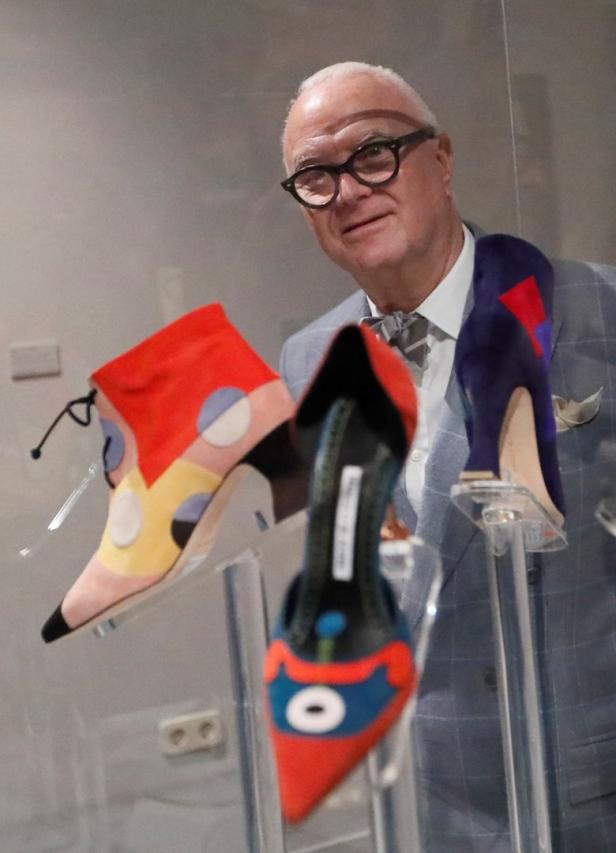Ein Mann mit Brille präsentiert farbenfrohe Damenschuhe auf transparenten Ständern.