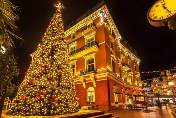 Ein großer, beleuchteter Weihnachtsbaum steht vor einem Gebäude in der Nacht.