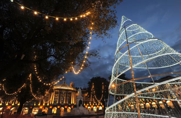 Ein beleuchteter Platz mit einem modernen Weihnachtsbaum und Lichterketten in der Dämmerung.