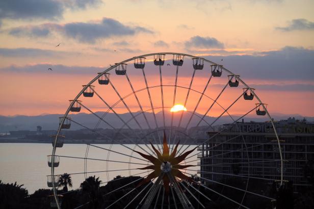 Ein Riesenrad vor einem Sonnenuntergang, mit Bergen im Hintergrund.