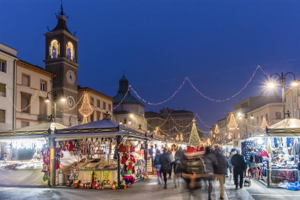 Ein Weihnachtsmarkt mit Buden und Lichtern in einer italienischen Stadt bei Dämmerung.