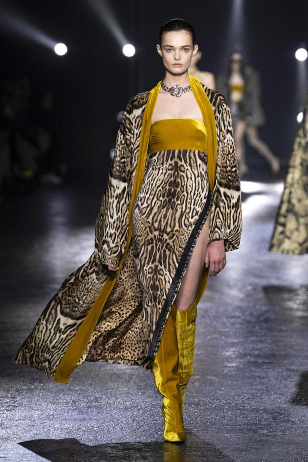 Ein Model auf dem Laufsteg trägt ein Kleid mit Tiermuster und goldene Stiefel.
