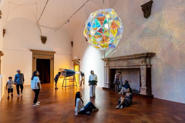 Besucher betrachten eine geometrische, farbige Glasinstallation in einem Ausstellungsraum.