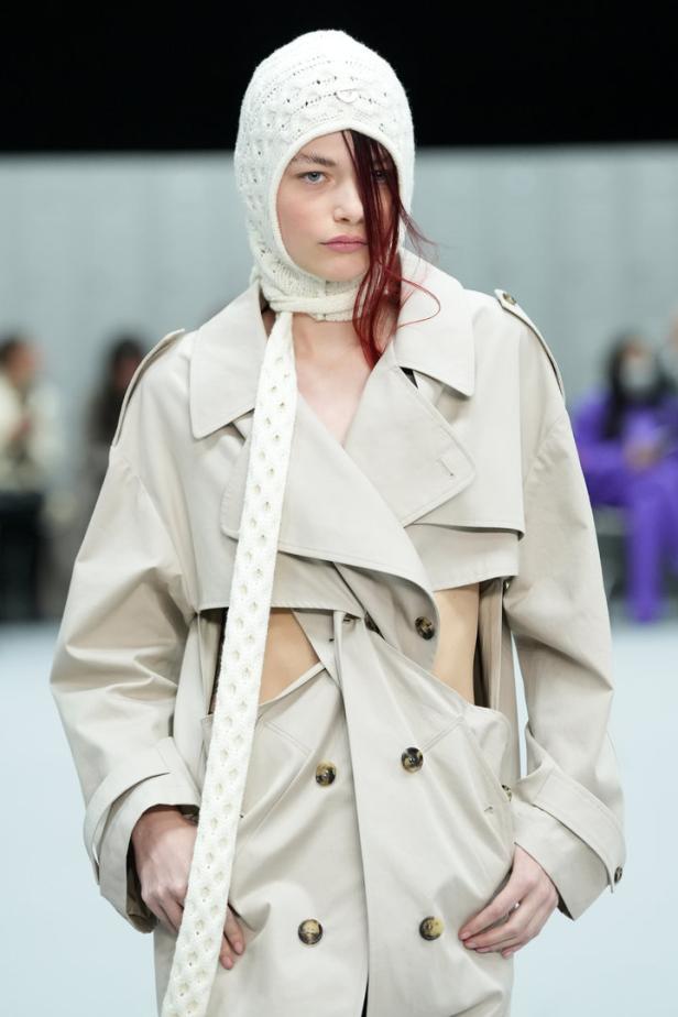 Eine Frau mit Strickmütze und Trenchcoat auf einem Laufsteg.