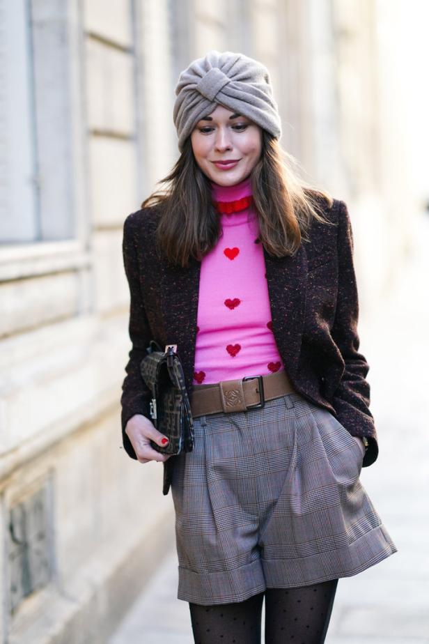 Eine Frau mit Turban, Blazer und Shorts mit Karomuster steht im Freien.