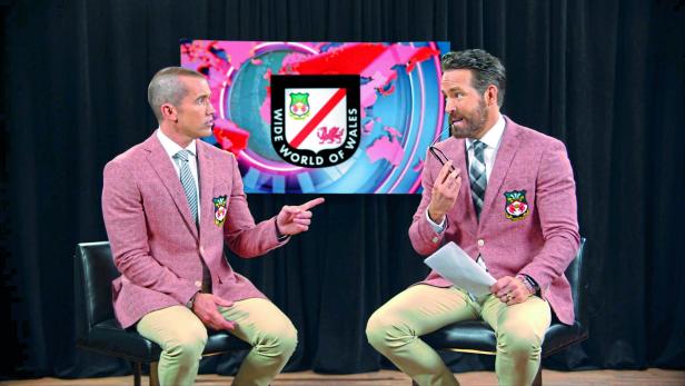 Ryan Reynolds und Rob McElhenney sitzen vor einem Bildschirm mit dem Logo „Wide World of Wales“.