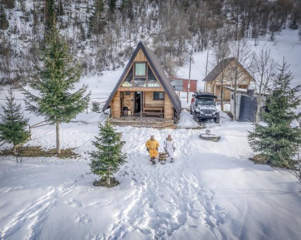 Ein Paar sitzt vor einem A-förmigen Holzhaus in einer verschneiten Winterlandschaft.