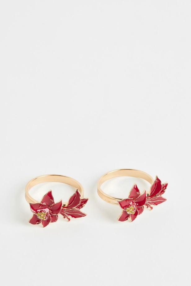 Zwei goldene Serviettenringe mit roten Blumenverzierungen liegen auf einem weißen Hintergrund.