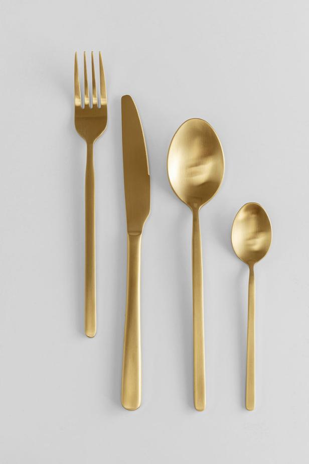 Ein goldenes Besteckset bestehend aus Gabel, Messer, Esslöffel und Teelöffel auf einem hellen Hintergrund.
