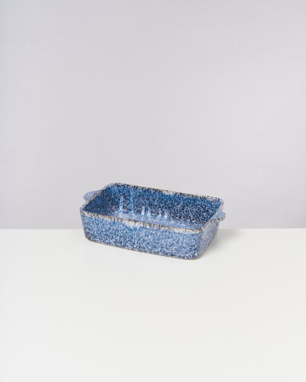 Eine rechteckige, blau gesprenkelte Auflaufform steht auf einem weißen Tisch.