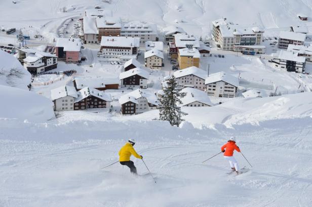 Skifahrer in Lech/Zürs vor verschneiten Häusern.