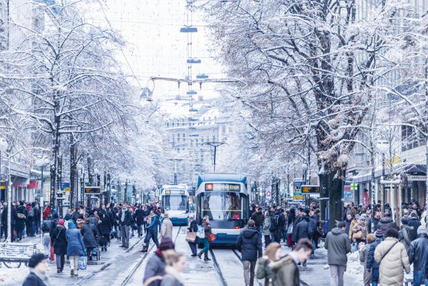 Eine verschneite Straße in Zürich mit Menschen und Straßenbahnen.