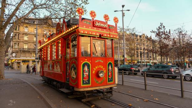 Eine rote, weihnachtlich dekorierte Straßenbahn der Marke „Jelmoli“ fährt durch Zürich.