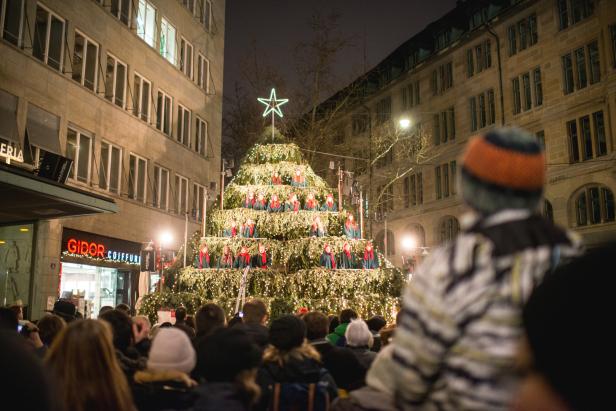 Ein Weihnachtschor singt auf einer pyramidenförmigen Bühne in der Stadt.