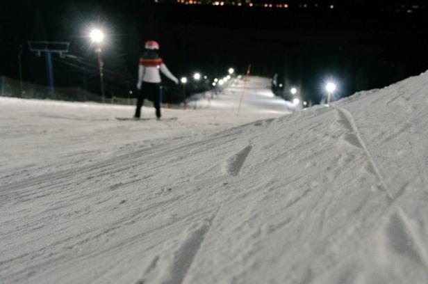 Eine Person fährt nachts auf einem Snowboard eine schneebedeckte Piste hinunter.