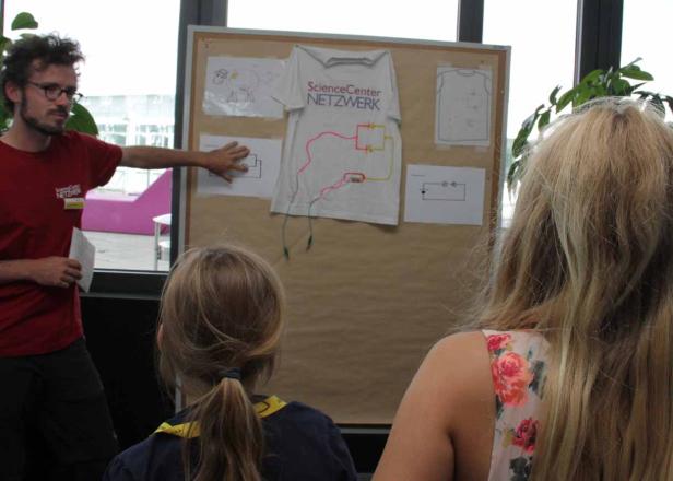 Ein Mann erklärt Kindern ein Experiment mit einem T-Shirt und Stromkreisen.