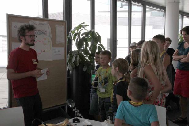 Ein Mann erklärt einer Gruppe von Kindern ein Projekt mit Schaltplänen.