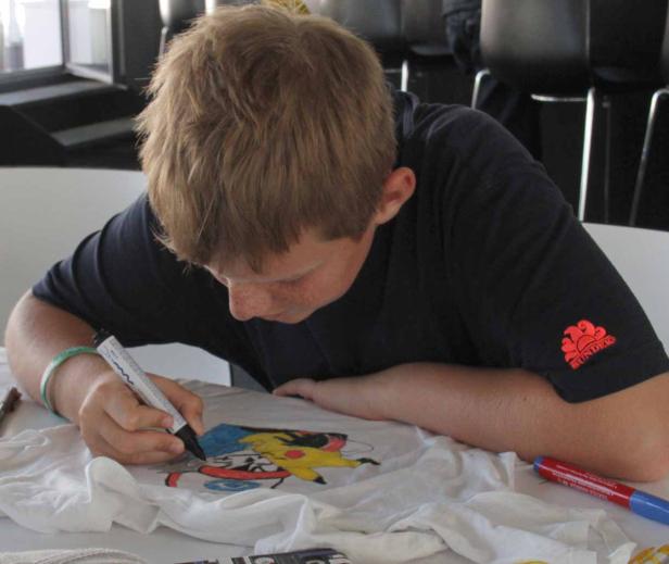 Ein Junge bemalt ein T-Shirt mit einem schwarzen Stift.