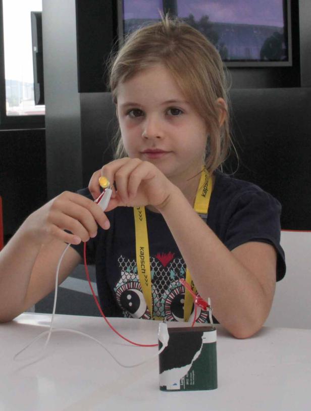 Ein Mädchen experimentiert mit einer Batterie, Kabeln und einer kleinen Glühbirne.