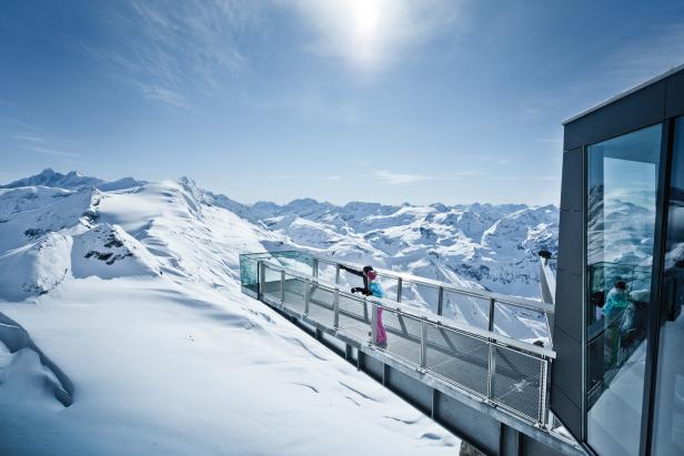 Eine Frau steht auf einer Aussichtsplattform in den schneebedeckten Bergen.