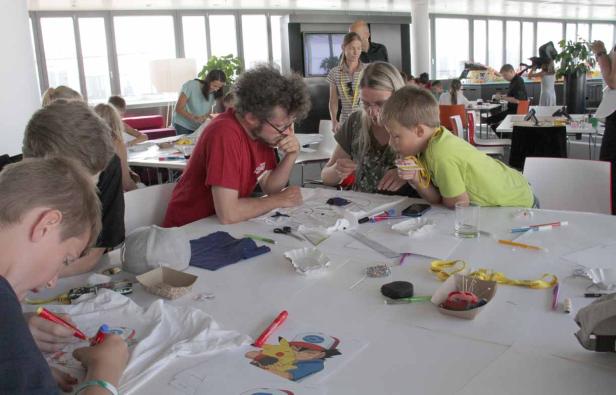 Kinder und Erwachsene gestalten gemeinsam T-Shirts an einem Tisch.
