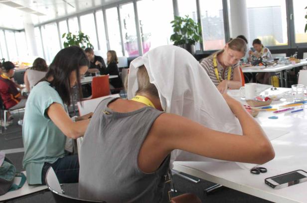 Mehrere Personen sitzen an Tischen und arbeiten an einem Projekt.