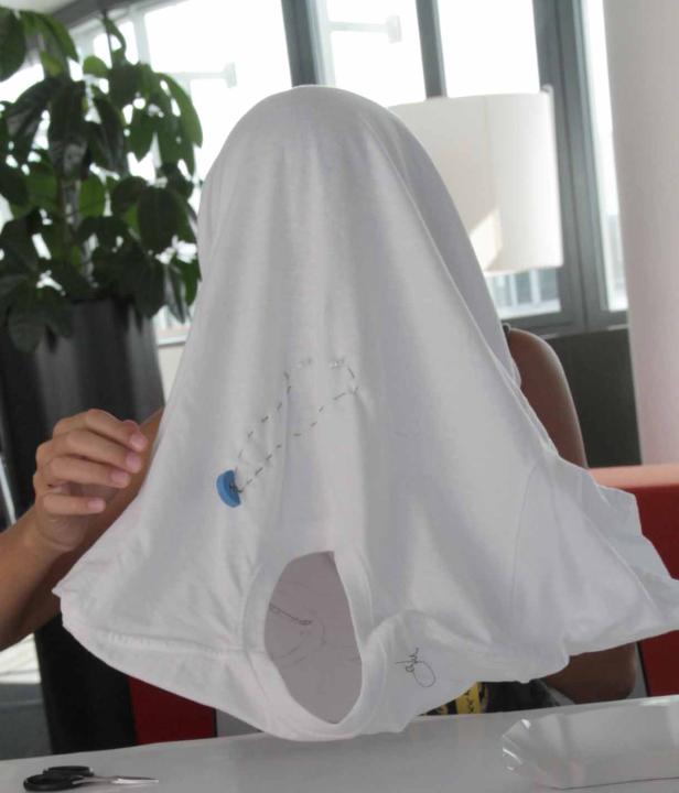 Eine Person hält ein weißes T-Shirt vor ihr Gesicht.