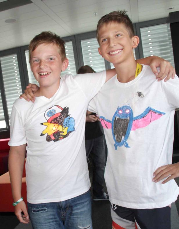 Zwei Jungen stehen nebeneinander und präsentieren stolz ihre selbstbemalten T-Shirts.