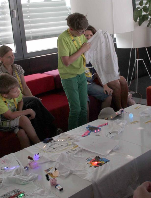 Eine Gruppe von Personen betrachtet T-Shirts mit elektronischen Bauteilen.