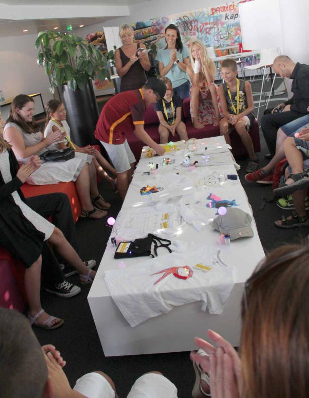 Eine Gruppe von Menschen betrachtet und applaudiert T-Shirts mit leuchtenden Dekorationen auf einem Tisch.