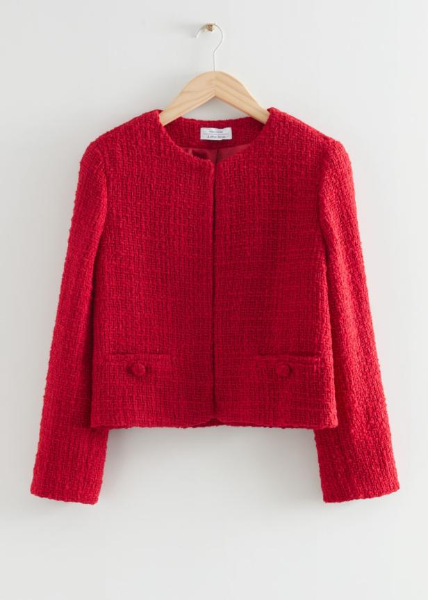 Eine rote Tweedjacke hängt an einem hölzernen Kleiderbügel vor einem weißen Hintergrund.
