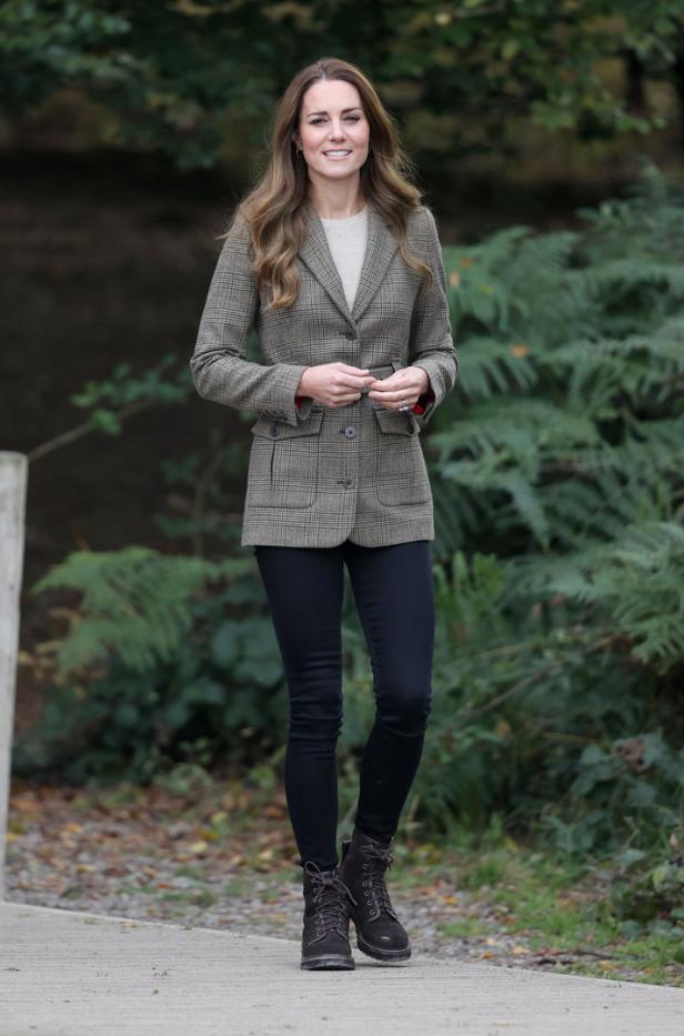Kate Middleton in einer Tweedjacke, schwarzen Jeans und Stiefeln in einer ländlichen Umgebung.