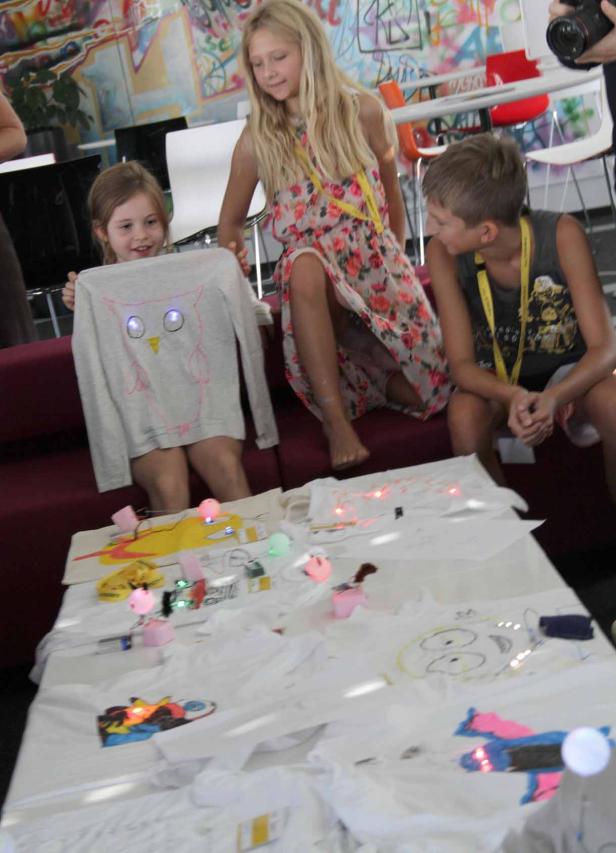Kinder präsentieren selbstgestaltete Kleidung mit leuchtenden Elementen.