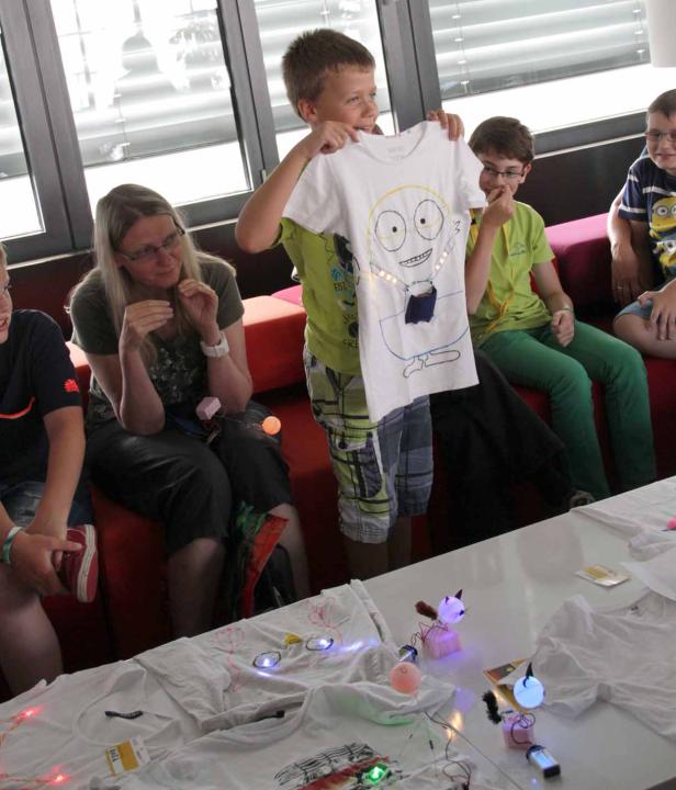 Ein Junge präsentiert stolz ein selbstbemaltes T-Shirt mit einem lustigen Monstergesicht.