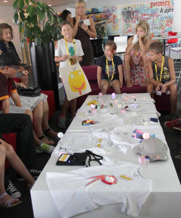 Kinder und Erwachsene sitzen um einen Tisch mit selbstgestalteten, leuchtenden T-Shirts.