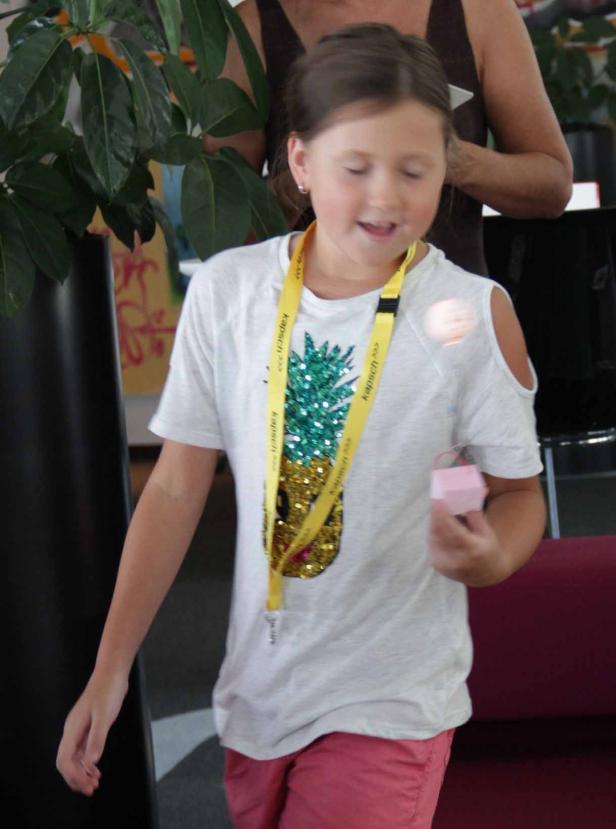 Ein junges Mädchen mit einem Ananas-T-Shirt hält eine kleine, rosa Schachtel.