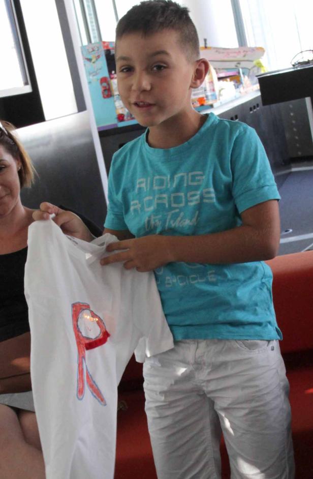 Ein Junge hält ein weißes T-Shirt mit einem roten „R“ darauf.