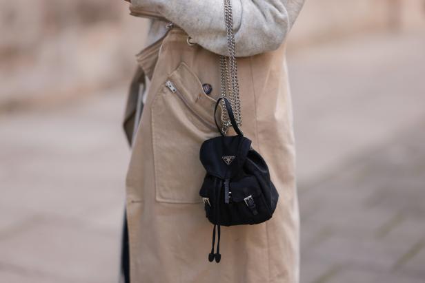 Eine Person trägt eine kleine schwarze Prada-Tasche an einer silbernen Kette.